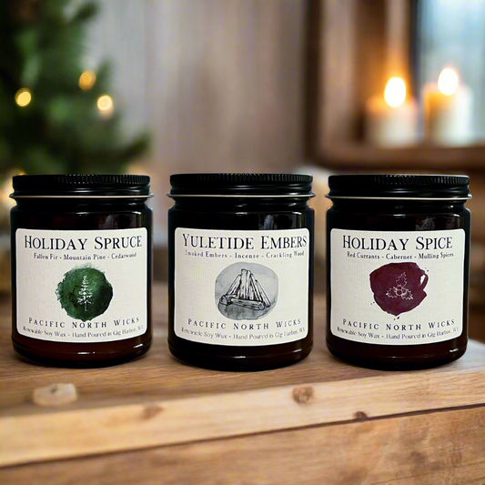 Three different scented holiday candles in glass jars, labeled as 'Holiday Spruce', 'Holiday Spice', and 'Yuletide Embers', arranged on a wooden surface with a blurred Christmas tree and candle lights in the background.