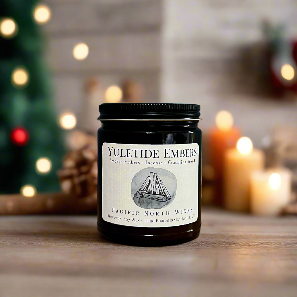Yuletide Embers Holiday Fireside Candle with Christmas lights blurred in background.