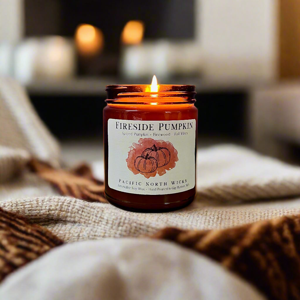 Pumpkin firewood candle burning in warm, rustic setting with cozy blankets and fall vibes
