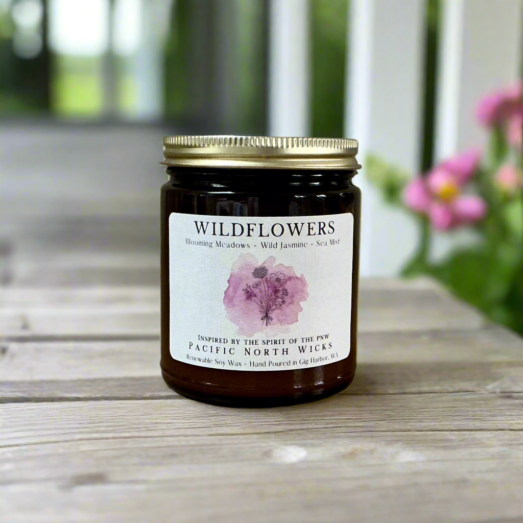 Wildflowers scented candle with gold lid in outdoor setting on farmhouse porch with pink flowers in background.