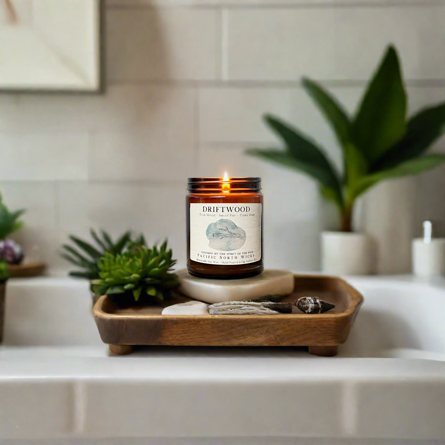 Driftwood Scented Candle lit in farmhouse bathroom with serene ambiance.  Candle is burning on rustic wooden bathtub tray with succulents and greenery around the tub.